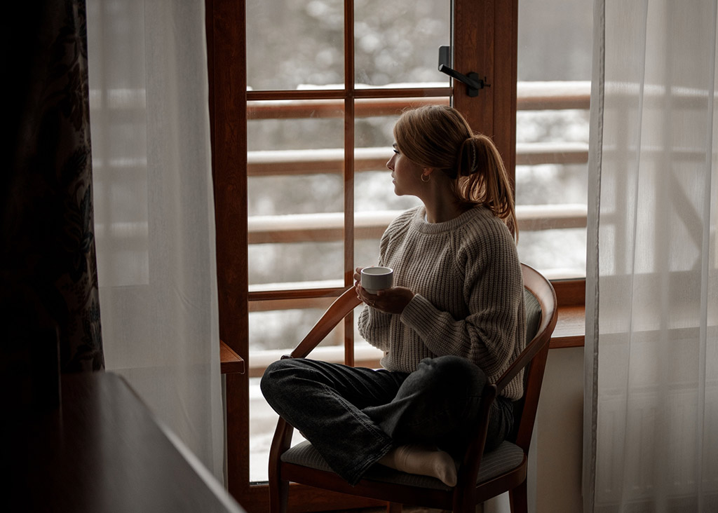 A woman sitting by the window as she watches the snow fall