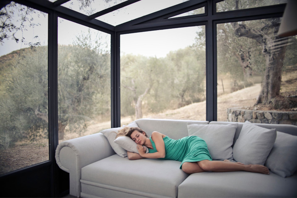 A woman asleep on a grey couch inside a sunroom