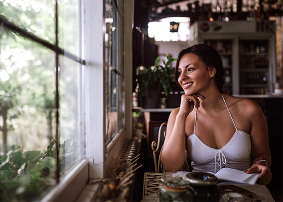 A woman sitting beside a window and gazing out the window with a smile 