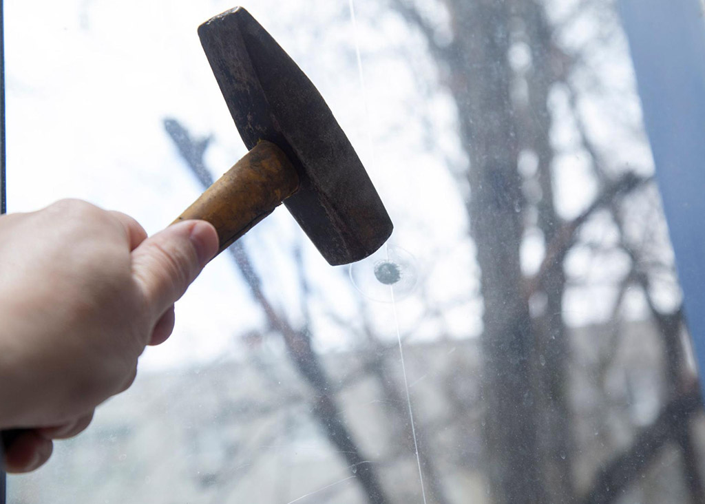 Close up of a hammer about to strike a window that has a security window film