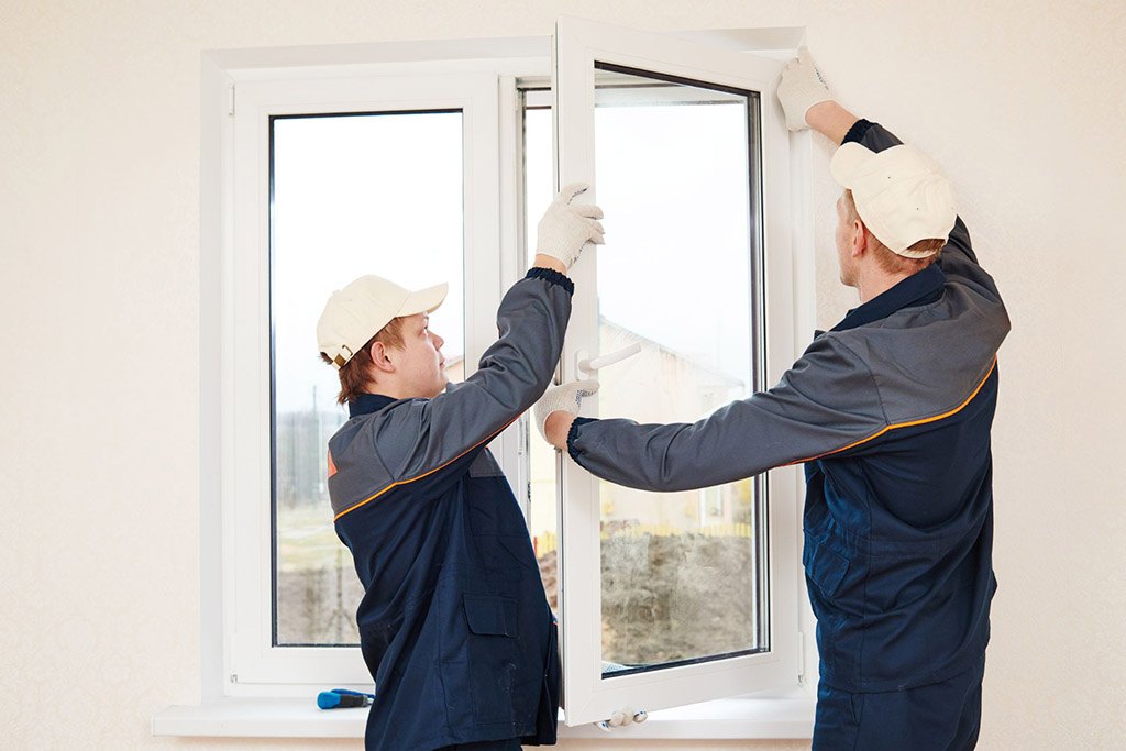 Two people dressed in uniforms installing a window with a white frame 