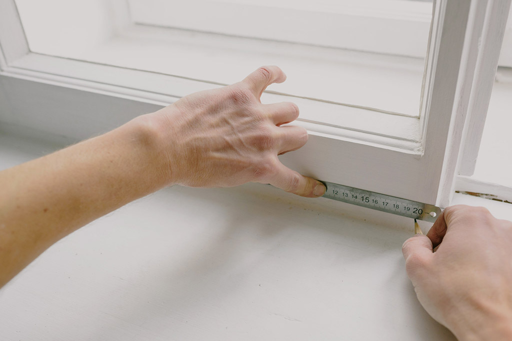 A pair of hands using a ruler and pencil to mark and measure the surface 